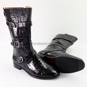May include: A pair of black crocodile leather boots with buckle straps. The boots have a pointed toe and a low heel.