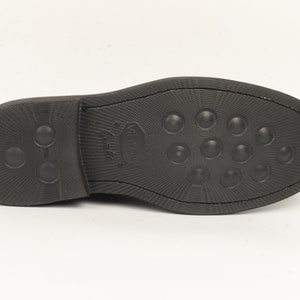 May include: The bottom of a black leather shoe with a textured sole and a small logo that says "Walk On" in white.