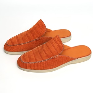 May include: A pair of orange leather slip-on shoes with a crocodile texture. The shoes have a rounded toe and a light-colored sole. The stitching is visible along the seams, and the interior is orange.