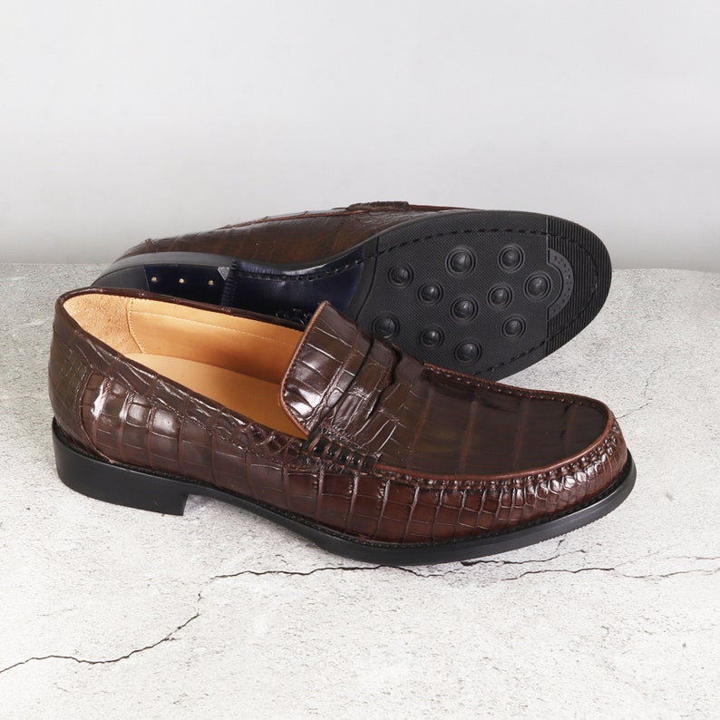 Puede incluir: Zapatos de vestir marrones de cuero con estampado de cocodrilo. Los mocasines tienen un dise&ntilde;o de deslizamiento y una suela de goma.