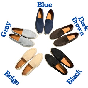 Op de afbeelding: Een selectie van herenslip-on schoenen in verschillende kleuren, waaronder blauw, grijs, beige, zwart en bruin. De schoenen zijn in een cirkel op een witte achtergrond gerangschikt.