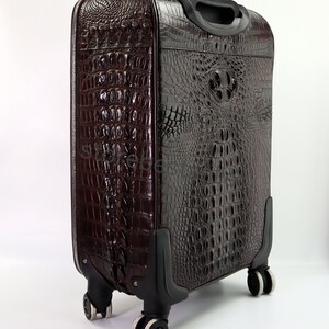 May include: A brown leather suitcase with a crocodile pattern. The suitcase has four wheels and a retractable handle.