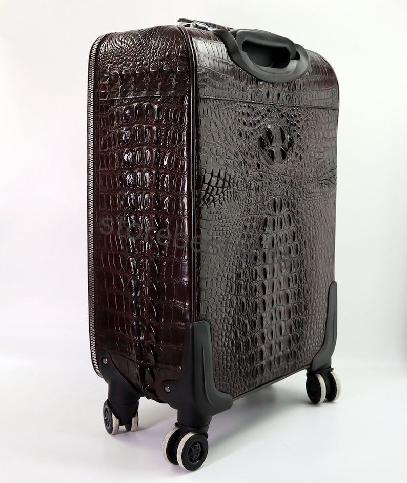May include: A brown leather suitcase with a crocodile pattern. The suitcase has four wheels and a retractable handle.