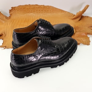May include: Two black leather lace-up shoes with a crocodile pattern. The shoes have a thick rubber sole.