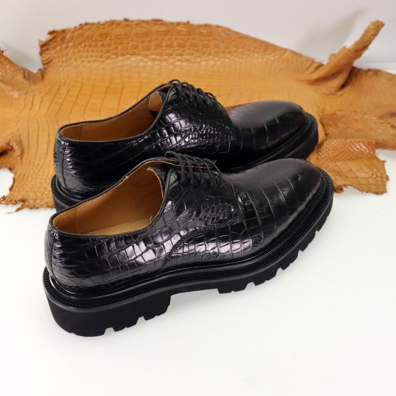 May include: Two black leather lace-up shoes with a crocodile pattern. The shoes have a thick rubber sole.