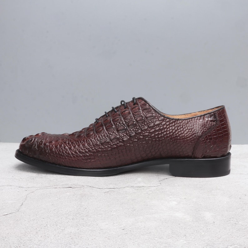 May include: A pair of burgundy leather lace-up shoes with a crocodile-embossed pattern.