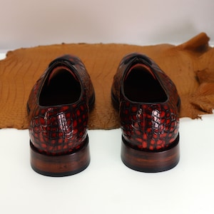 May include: A pair of red and black leather shoes with a crocodile pattern. The shoes have a brown leather sole and a lace-up closure.