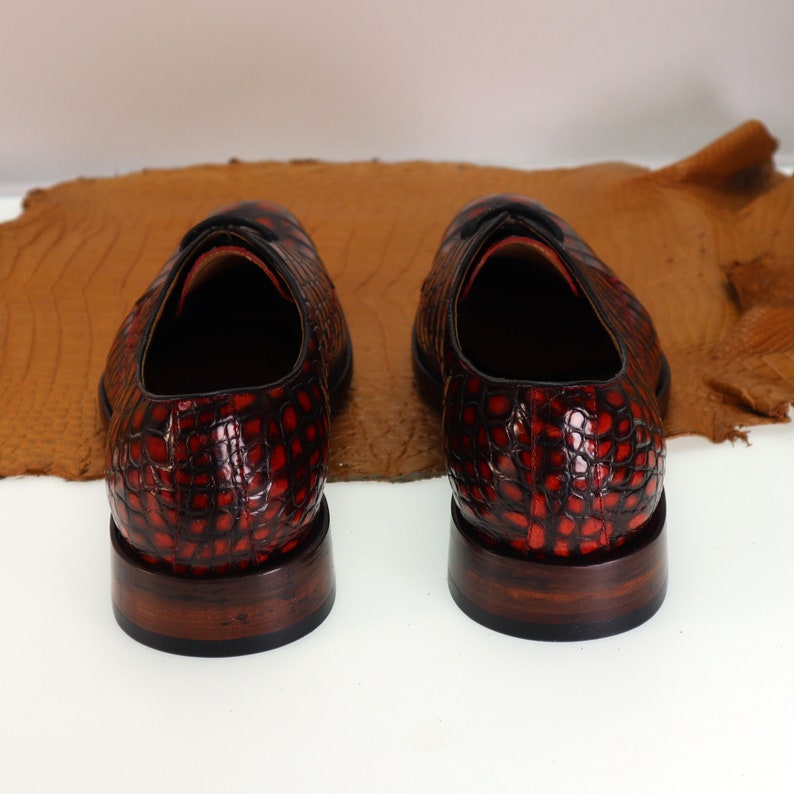 May include: A pair of red and black leather shoes with a crocodile pattern. The shoes have a brown leather sole and a lace-up closure.