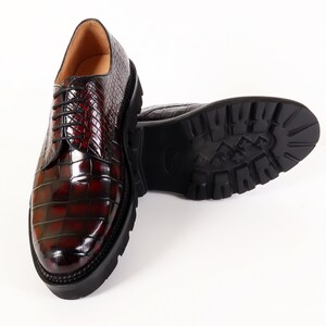 May include: A pair of dark red leather shoes with a crocodile pattern. The shoes have a lace-up closure and a thick, black rubber sole.