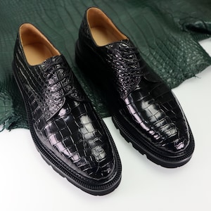 May include: A pair of black leather lace-up shoes with a crocodile pattern. The shoes have a thick sole and a rounded toe.