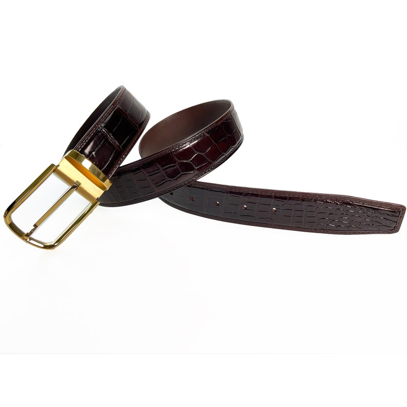May include: A brown leather belt with a gold buckle. The belt is made of crocodile skin and has a smooth finish.
