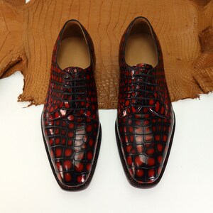 May include: A pair of black leather dress shoes with a red crocodile pattern. The shoes have a lace-up closure and a pointed toe.