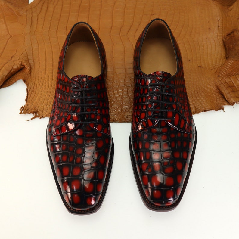 May include: A pair of black leather dress shoes with a red crocodile pattern. The shoes have a lace-up closure and a pointed toe.