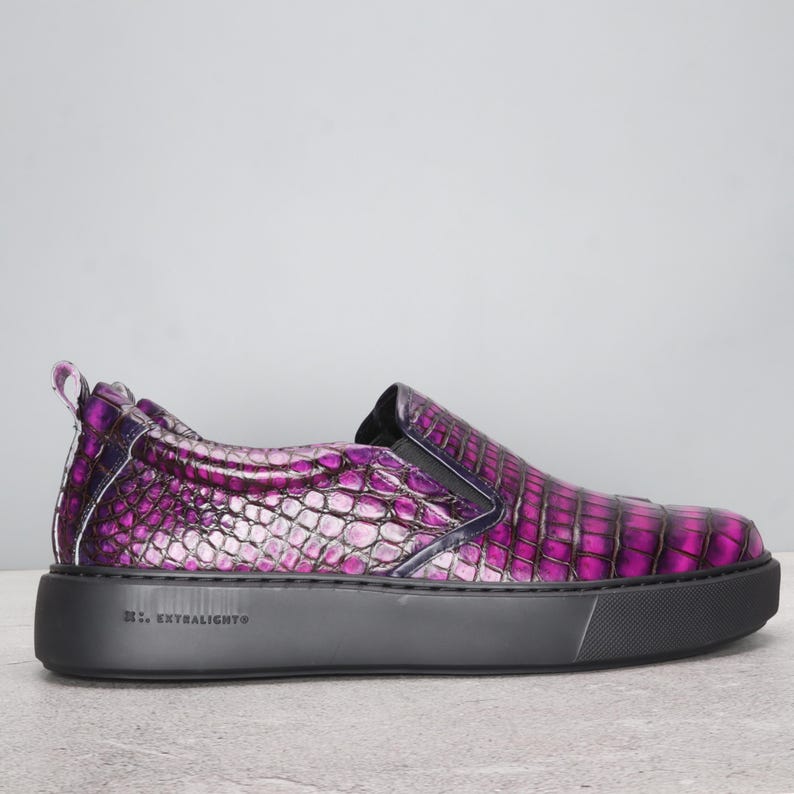 May include: A slip-on shoe with a textured, purple and pink snakeskin pattern. The shoe has a black sole and a small pull tab at the heel. The text "EXTRA LIGHT" is printed on the side of the sole.