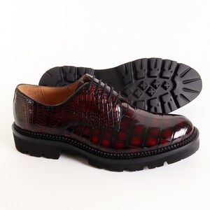 May include: A pair of burgundy leather lace-up shoes with a crocodile-embossed pattern. The shoes have a thick black rubber sole.