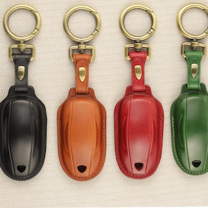 May include: Four leather keychains with different colored leather covers: black, brown, red, and green. Each keychain has a gold metal ring and a gold metal hook.
