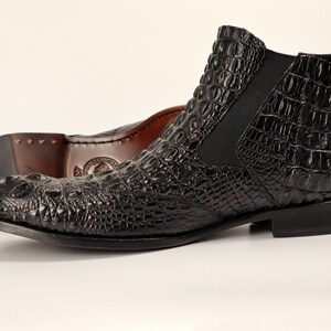May include: Black leather ankle boots with a crocodile pattern. The boots have a pointed toe and a low heel.
