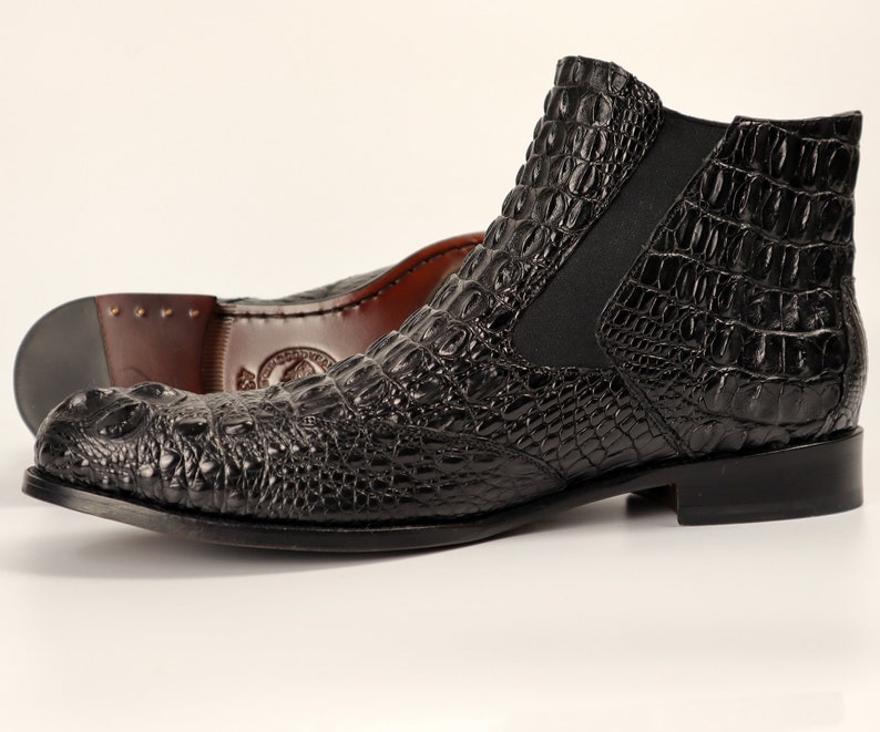 May include: Black leather ankle boots with a crocodile pattern. The boots have a pointed toe and a low heel.