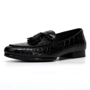 May include: Black leather loafer with a textured, crocodile-like pattern. The shoe features a tassel detail and a low heel. The design is sleek and classic, suitable for formal or semi-formal occasions.
