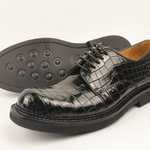 May include: Black leather lace-up shoes with a crocodile pattern. The shoes have a thick sole and a rounded toe.