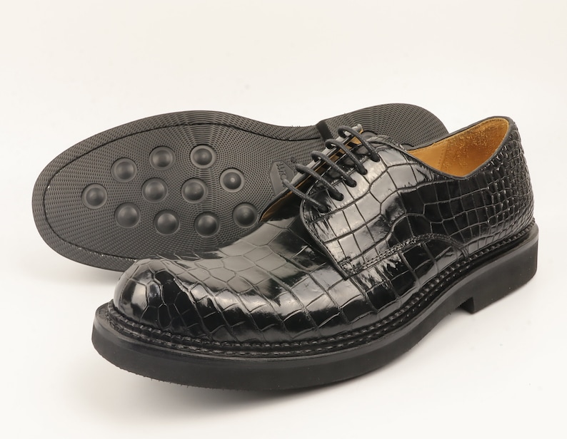 May include: Black leather lace-up shoes with a crocodile pattern. The shoes have a thick sole and a rounded toe.
