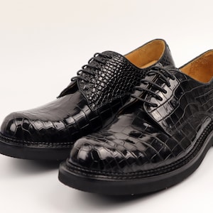 May include: A pair of black leather lace-up shoes with a crocodile pattern. The shoes have a thick sole and a rounded toe.