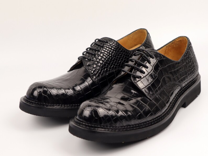 May include: A pair of black leather lace-up shoes with a crocodile pattern. The shoes have a thick sole and a rounded toe.