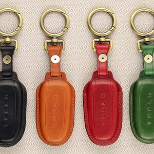 May include: Four leather keychains with metal key rings and the word "TESLA" embossed on the front. The keychains are black, brown, red, and green.