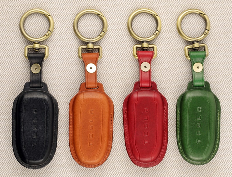 May include: Four leather keychains with metal key rings and the word "TESLA" embossed on the front. The keychains are black, brown, red, and green.