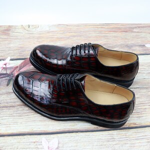 Peut inclure: Une paire de chaussures en cuir marron &agrave; lacets avec un motif crocodile. Les chaussures ont une semelle noire et une doublure en cuir marron.