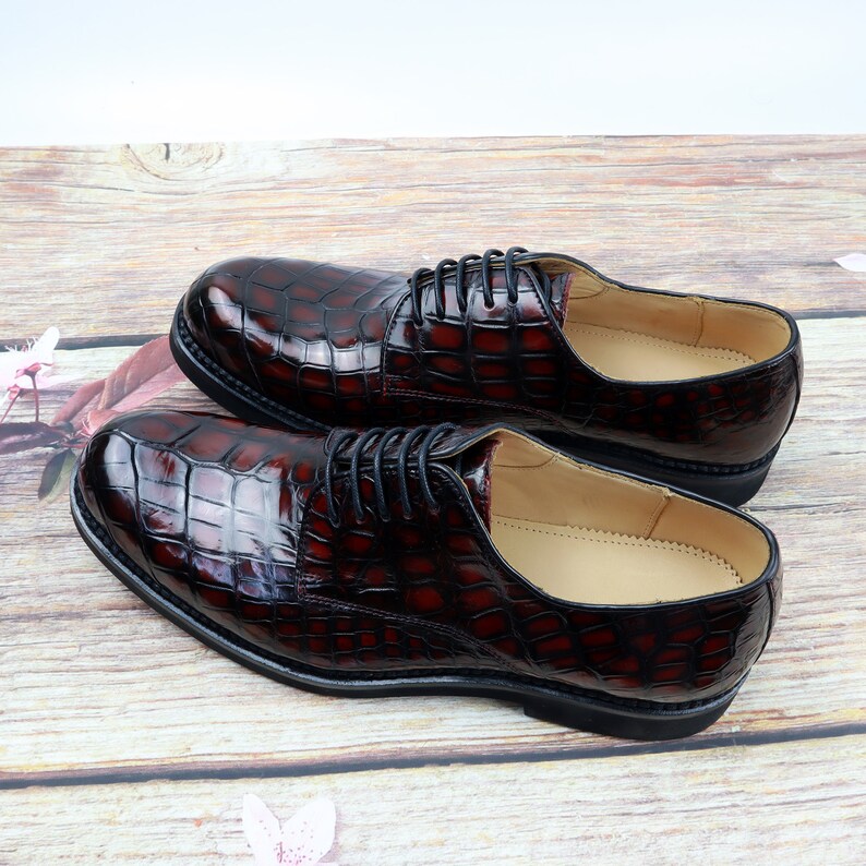Peut inclure: Une paire de chaussures en cuir marron &agrave; lacets avec un motif crocodile. Les chaussures ont une semelle noire et une doublure en cuir marron.