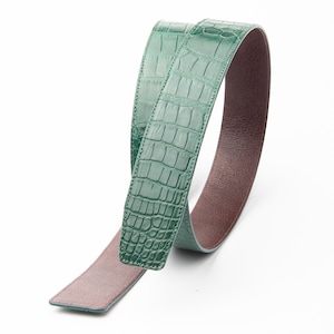 May include: A green crocodile leather belt with a brown leather backing. The belt is folded in half and the green side is facing the camera.