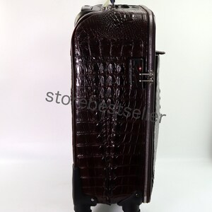 May include: A brown crocodile embossed leather suitcase with a black handle and wheels. The suitcase has a zipper closure and a combination lock.