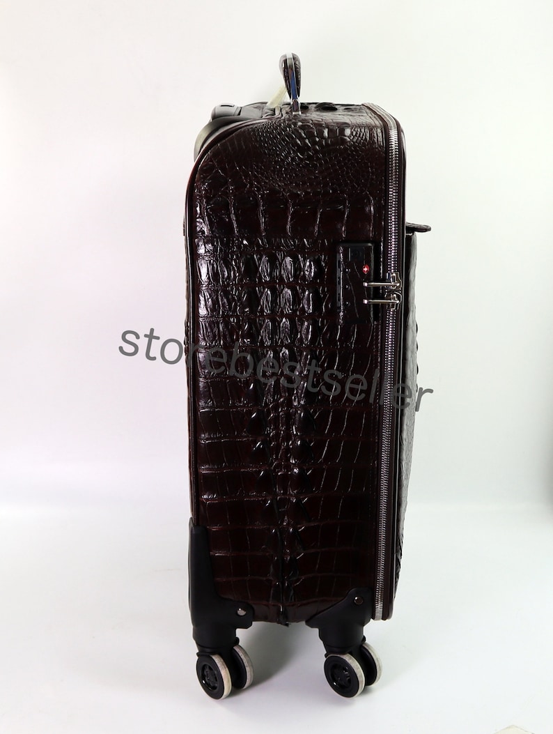 May include: A brown crocodile embossed leather suitcase with a black handle and wheels. The suitcase has a zipper closure and a combination lock.