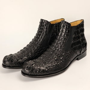 May include: A pair of black leather ankle boots with a crocodile pattern. The boots have a pointed toe and a low heel.