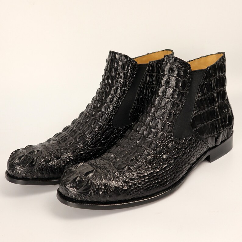 May include: A pair of black leather ankle boots with a crocodile pattern. The boots have a pointed toe and a low heel.