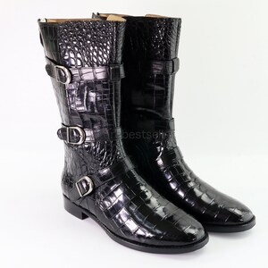 May include: Black leather boots with a crocodile pattern and multiple buckles. The boots have a pointed toe and a low heel.