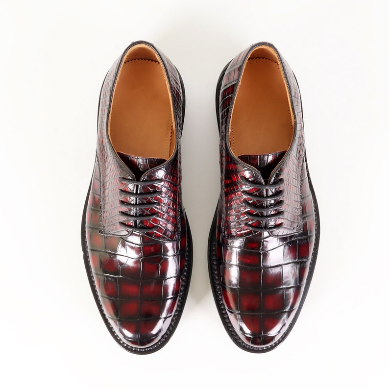 May include: A pair of burgundy leather lace-up shoes with a crocodile pattern.