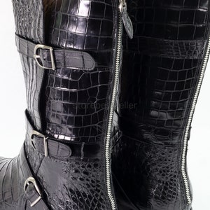 May include: Black leather boots with a crocodile pattern and multiple buckles. The boots have a zipper on the side.