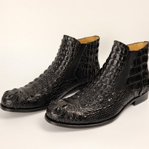 May include: A pair of black leather ankle boots with a crocodile pattern. The boots have a pointed toe and a low heel.