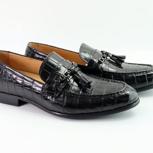 May include: A pair of black leather loafers with a crocodile pattern and tassel accents. The loafers have a pointed toe and a low heel.