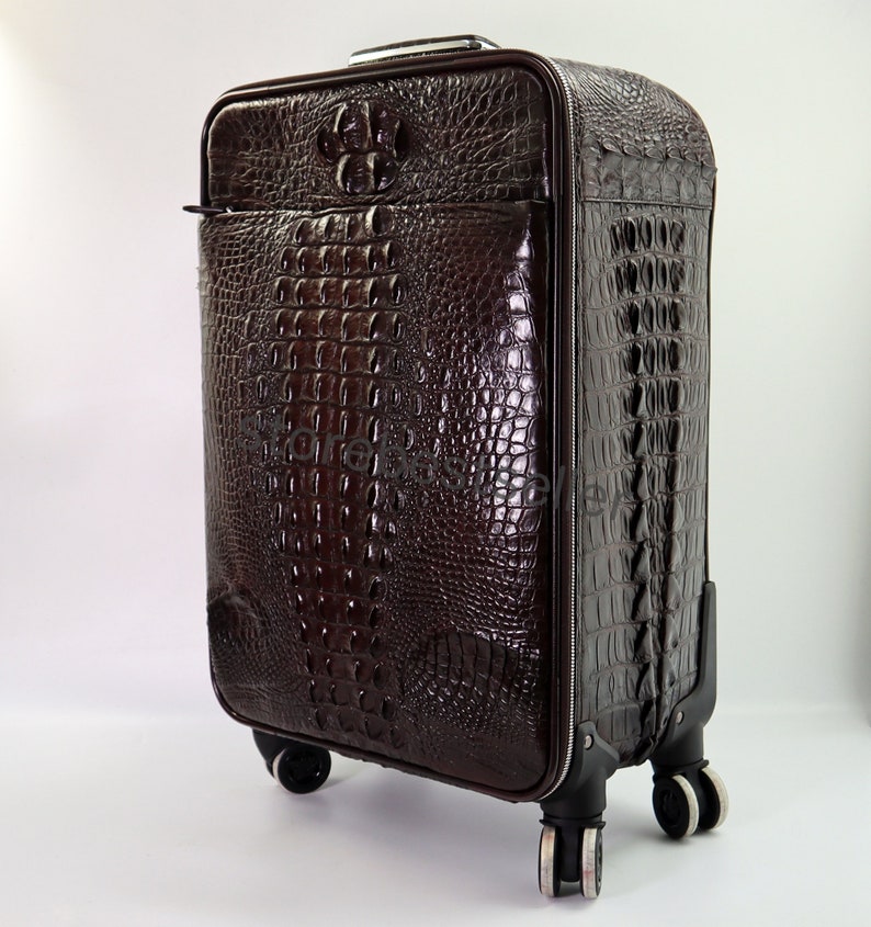 May include: A brown leather suitcase with a crocodile pattern. The suitcase has four wheels and a retractable handle.
