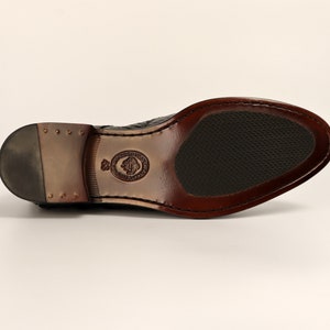 May include: Black leather dress shoe with a brown sole and a textured pattern. The shoe has a small logo on the side.
