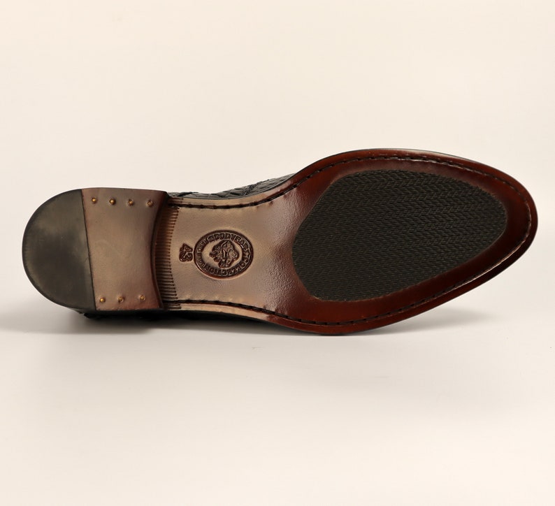 May include: Black leather dress shoe with a brown sole and a textured pattern. The shoe has a small logo on the side.