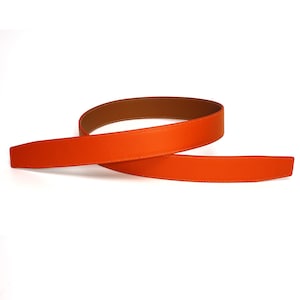 May include: An orange leather belt with a brown interior and white stitching. The belt is shown in a curved shape against a white background. The belt is approximately 1.25 inches wide.