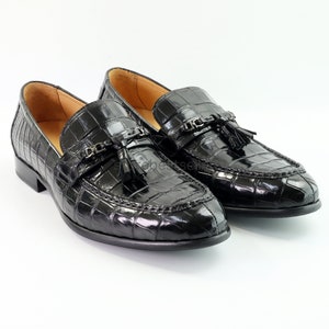 May include: A pair of black leather loafers with a crocodile pattern and tassel accents. The loafers have a pointed toe and a low heel.