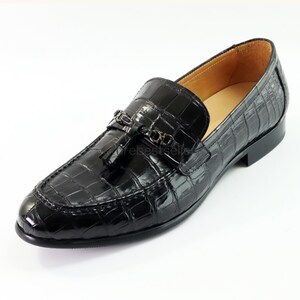 May include: Black leather loafers with a crocodile pattern and a tassel detail. The loafers have a silver buckle with a decorative design.
