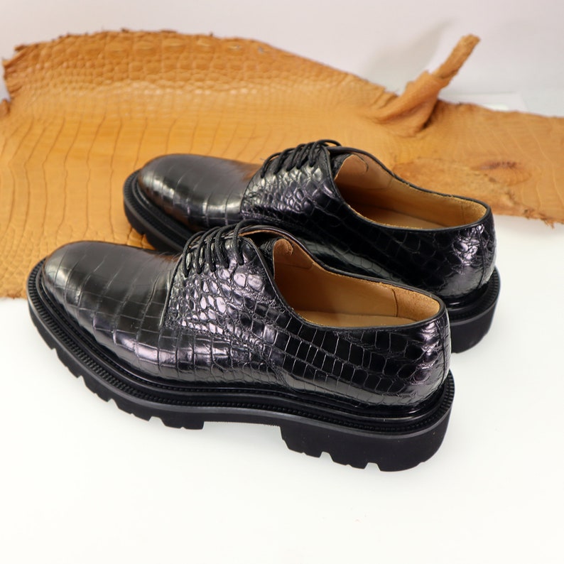 May include: A pair of black leather lace-up shoes with a crocodile pattern. The shoes have a thick rubber sole.