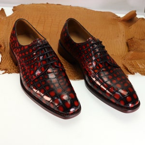 May include: A pair of red and black crocodile leather dress shoes with lace-up closures.