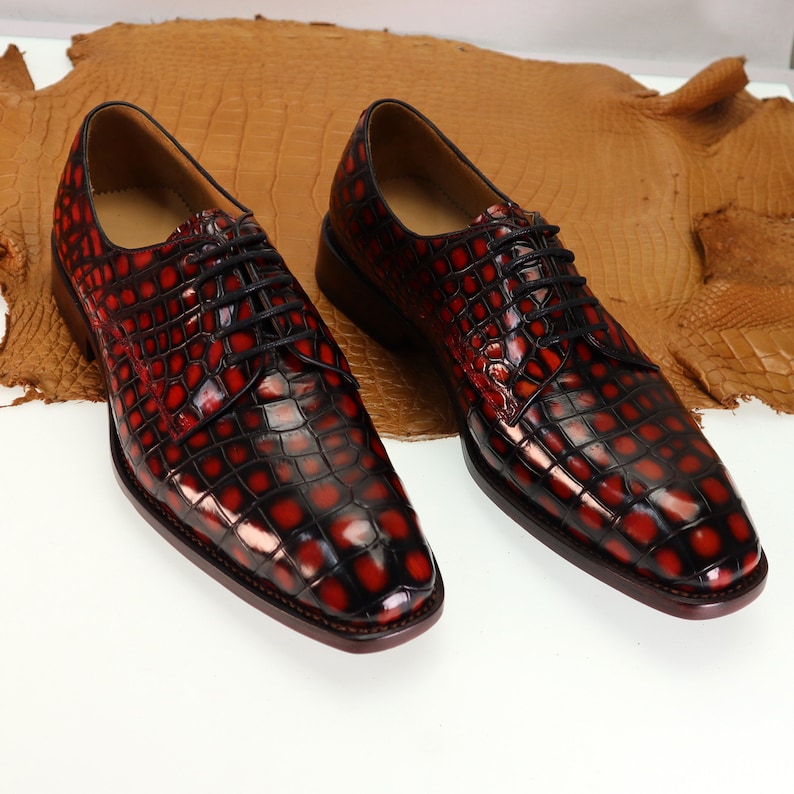 May include: A pair of red and black crocodile leather dress shoes with lace-up closures.